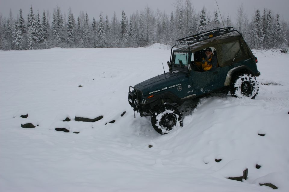Green Jeep Wrangler 4x4 driving through snow with roof rack