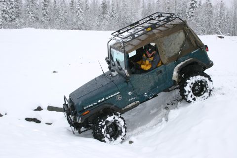 2003 Jeep TJ - Driver navigates a 2003 Jeep TJ through a snowy landscape with trees in the background.