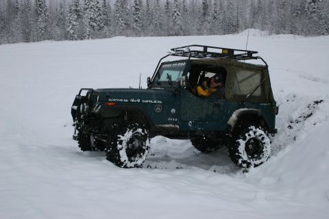 2003 Jeep TJ - A Jeep Wrangler YJ navigates a snowy trail with a driver wearing a yellow jacket.