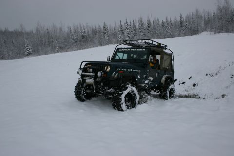 2003 Jeep TJ - A Jeep Wrangler navigates a snowy terrain with a wooded background.