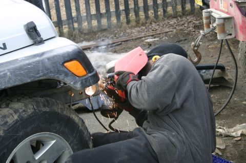 2003 Jeep TJ - A person welds the front fender of a white 2003 Jeep TJ, with sparks flying.