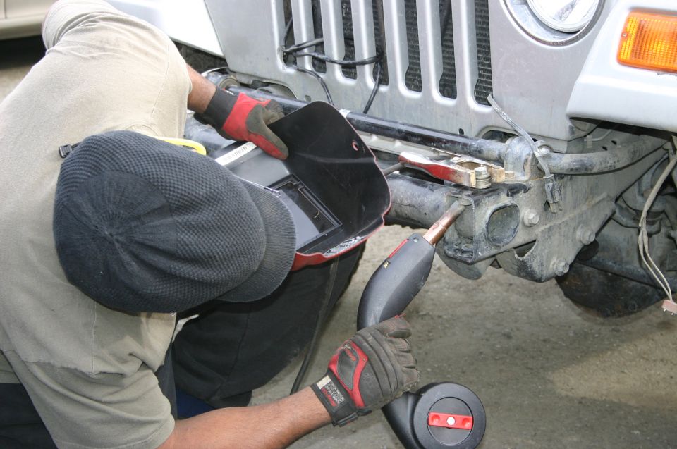 Man welding a bracket on a 2003 Jeep TJ front bumper