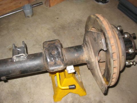 1995 Ford Bronco - Close-up of a vehicle's rear axle assembly, including the brake rotor and caliper bracket, supported by a yellow jack stand.