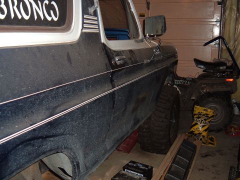 1979 Ford Bronco - The side profile of a dark blue 1979 Ford Bronco is visible, parked next to an ATV in a garage.
