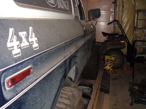 1979 Ford Bronco - The side profile of a blue 1979 Ford Bronco, prominent 4x4 badging, is visible in a garage setting.