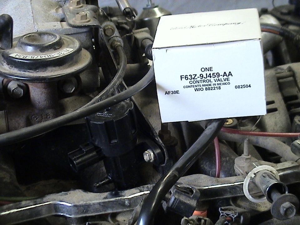 Ford control valve part in box marked F63Z-9J459-AA sitting on a disassembled engine intake