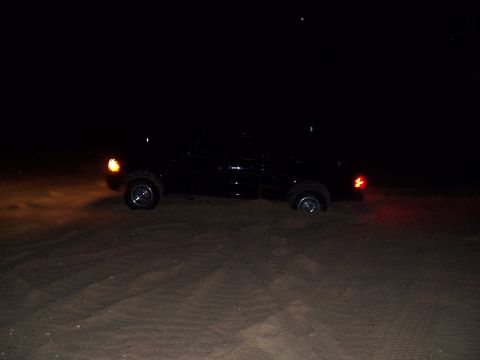 2003 Ford Ranger - A black pickup truck is stuck in the sand at night, with its tires partially submerged.