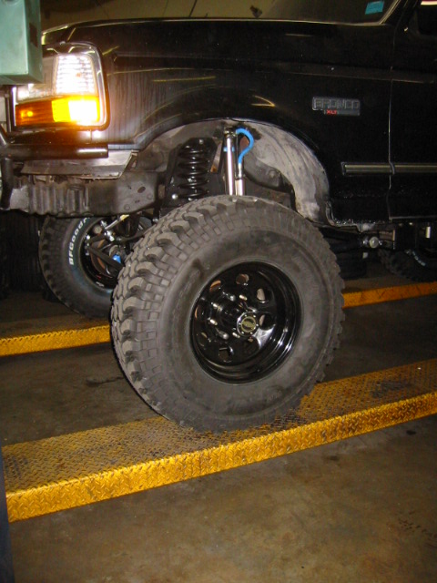 1992 Ford Bronco - A black Ford Bronco is shown with its front wheel and lifted suspension, positioned on yellow ramps.