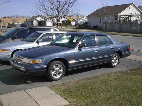 1985 Mercury Grand Marquis - A dark blue Mercury Grand Marquis is parked on a driveway next to another car.