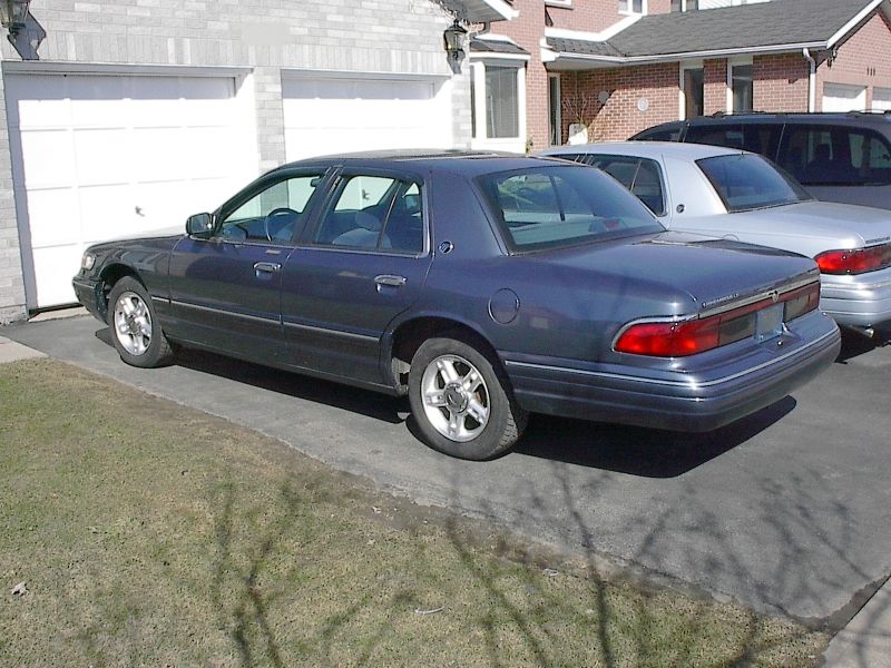 Slate blue Grand Marquis sedan parked on a driveway, rear three-quarter view