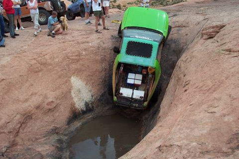 1990 Ford Bronco - Off-road vehicle stuck in a tight spot on a rocky trail with onlookers.