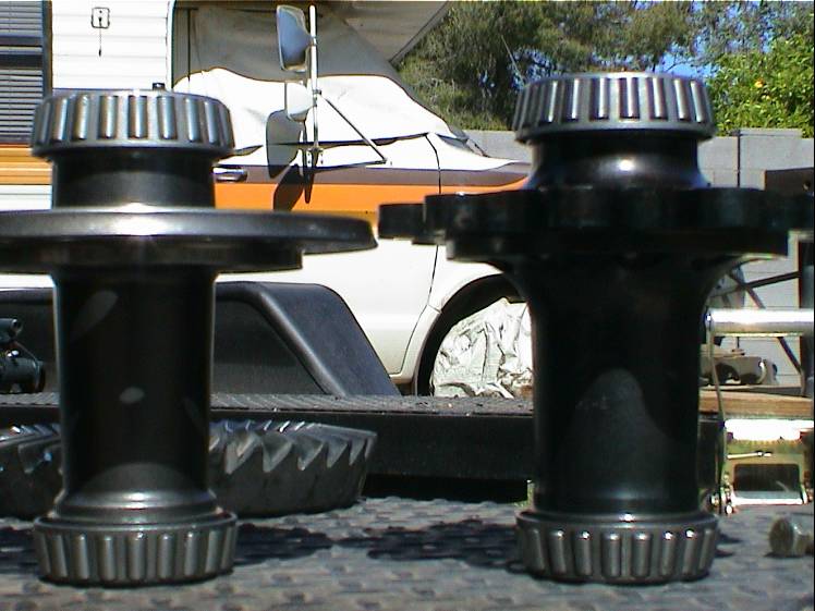 Two differential bearing and race sets in foreground. A covered vehicle with orange stripe and a trailer are in the background