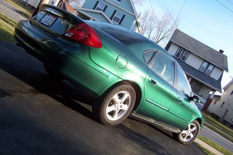 2000 Ford Taurus - A green sedan is parked in front of houses on a sunny day. The car's rear and side are visible.