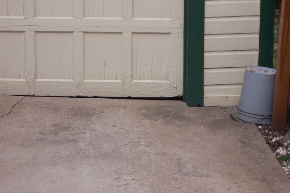 Garage door and concrete driveway with a gray bucket