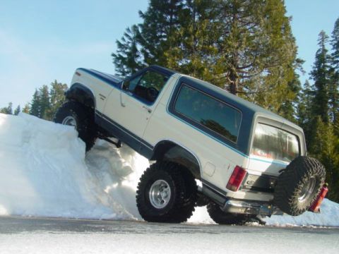 1986 Ford Bronco - A lifted Ford Bronco navigates a steep snowbank, its off-road capabilities.