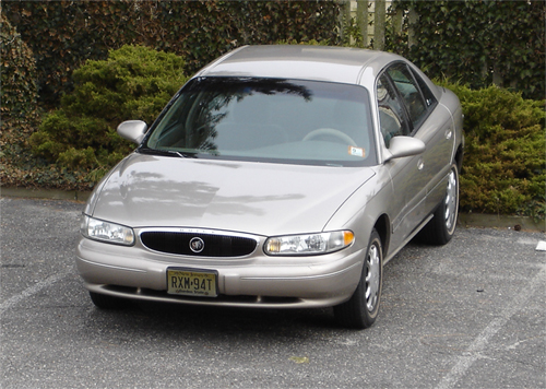Tan Buick Century sedan, front three-quarter, parked in front of dark hedges on pavement