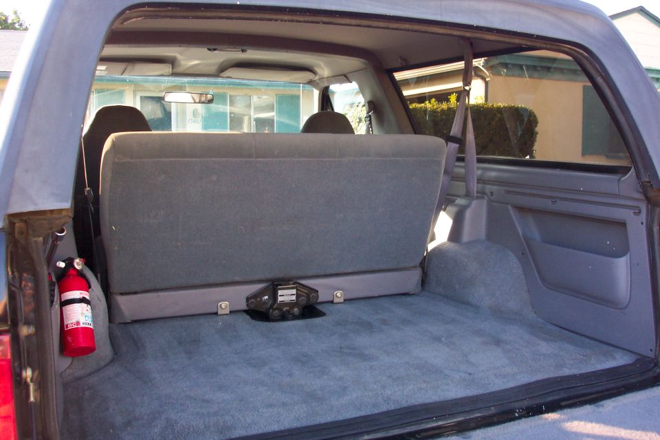 Rear cargo area of an SUV with gray folding bench seat and a red fire extinguisher mounted at left