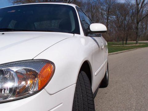 2001 Ford Taurus - A white sedan is parked on the side of a road with trees in the background under a clear blue sky.