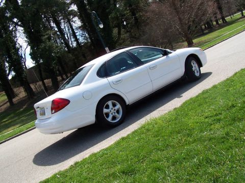2001 Ford Taurus - A white sedan is parked on the side of a road with green grass and trees in the background.