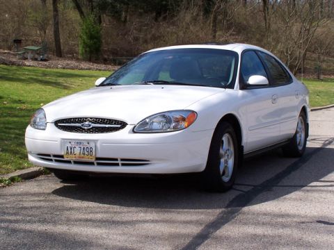2001 Ford Taurus - White Ford Taurus sedan parked on a paved surface with trees in the background.