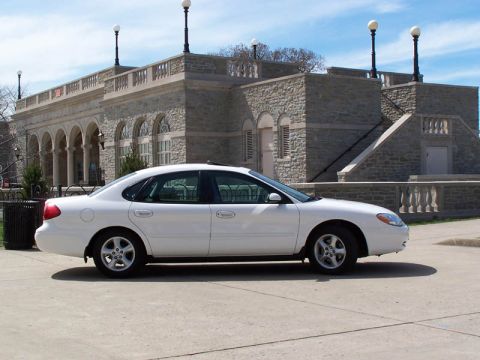 2001 Ford Taurus - A white sedan is parked in front of a stone building with arched windows and decorative lamps.