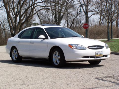 2001 Ford Taurus - A white sedan is parked on a paved surface with trees and a stop sign in the background.