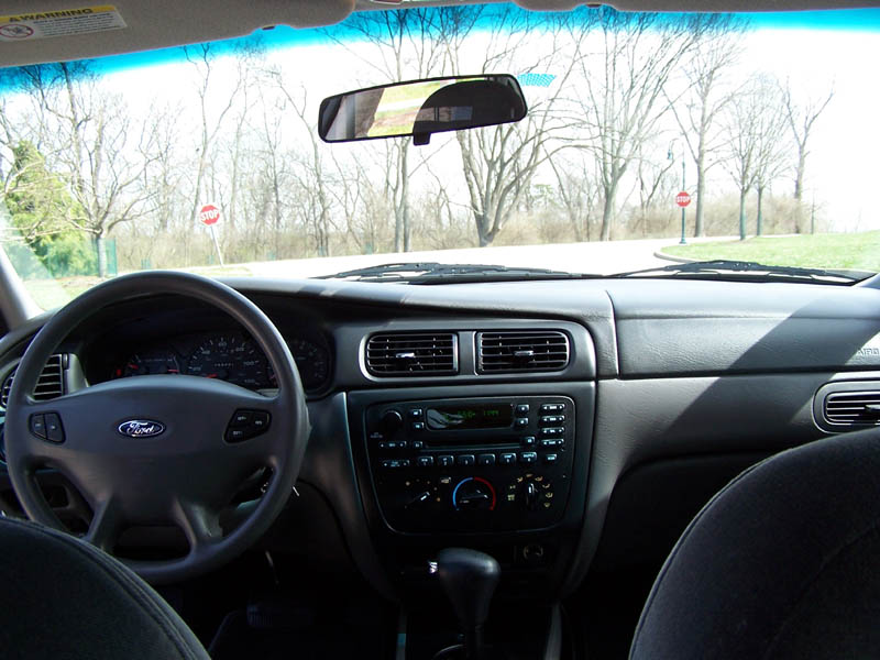 Car interior showing dashboard, steering wheel with Ford logo, and center console
