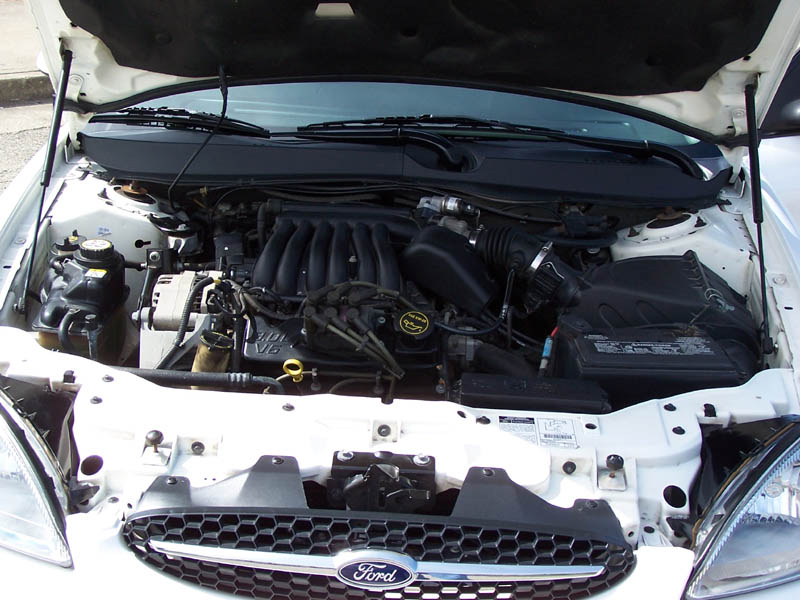 Ford V6 engine bay with intake manifold and exposed core support, Ford-badged grille below