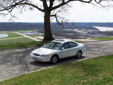 2001 Ford Taurus - A white sedan is parked on a road overlooking an airport and a body of water.