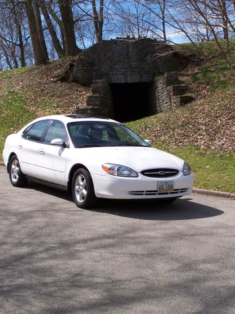 2001 Ford Taurus - A white 2001 Ford Taurus is seen parked on a paved surface in front of a stone tunnel and grassy hill.