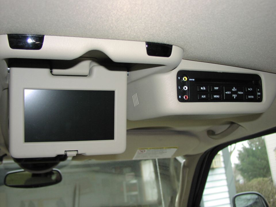 Ceiling-mounted DVD entertainment system with fold-down screen in a tan vehicle headliner