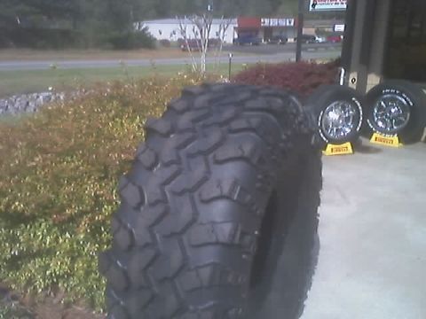 1976 Ford F-150 - A large off-road tire is prominently displayed in front of two chrome wheels mounted on yellow stands.