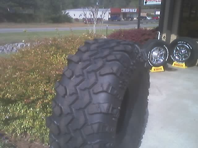 Off-road tire in foreground, two chrome wheels with yellow stands behind