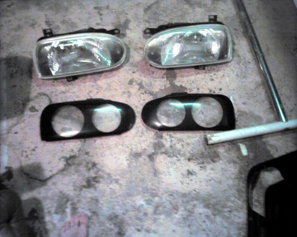 Two car headlights and two black bezels with double circular cutouts on a concrete floor