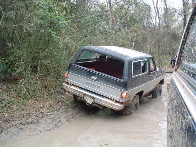 Black and tan Chevrolet K5 Blazer driving through mud, rear view