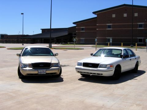 2000 Ford Crown Victoria - Two Ford Crown Victorias are parked side-by-side in a paved lot with a building in the background.