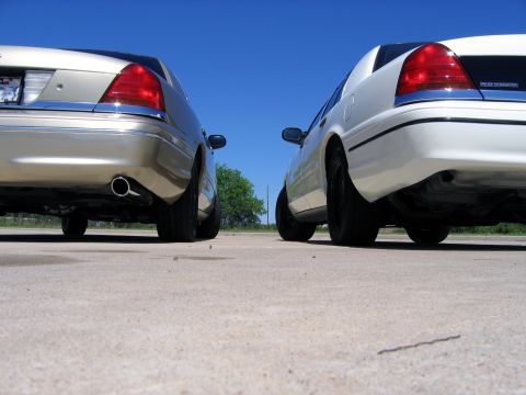 2000 Ford Crown Victoria - Two Ford Crown Victorias are parked side-by-side on a paved surface under a clear blue sky.