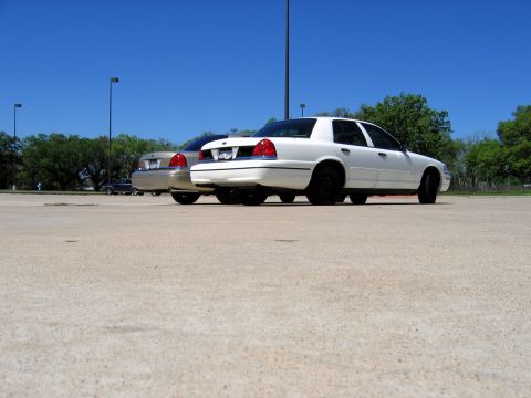 2000 Ford Crown Victoria - Two white 2000 Ford Crown Victorias are parked in a lot, viewed from the rear.