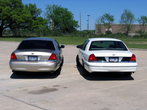 2000 Ford Crown Victoria - Two Ford Crown Victorias are parked in a lot under a clear blue sky.