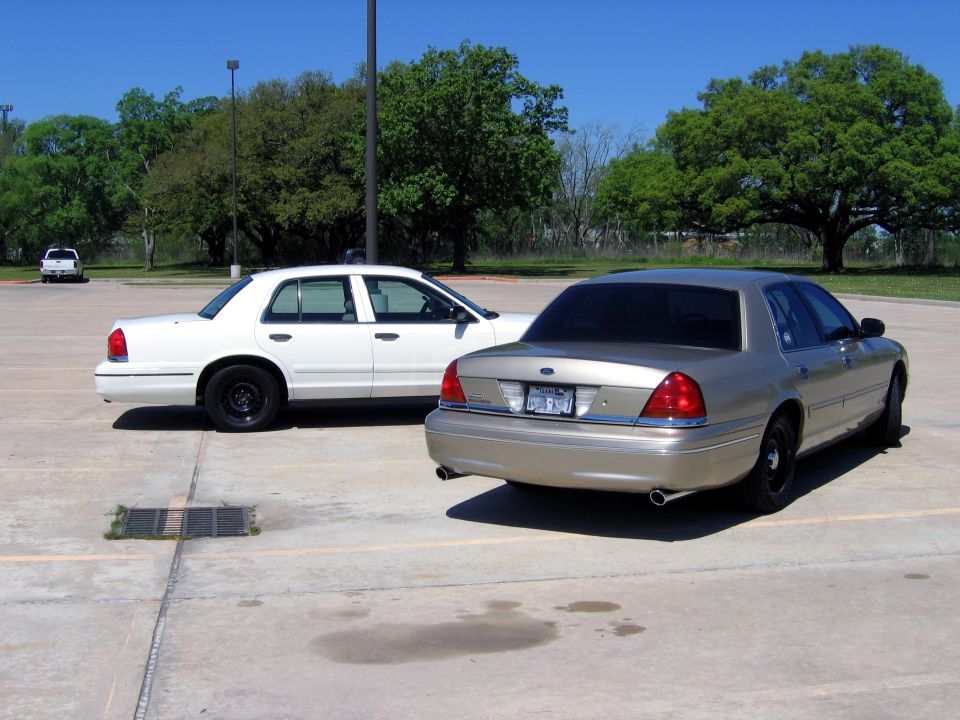 Two police sedans parked in a lot. One is white, the other is tan