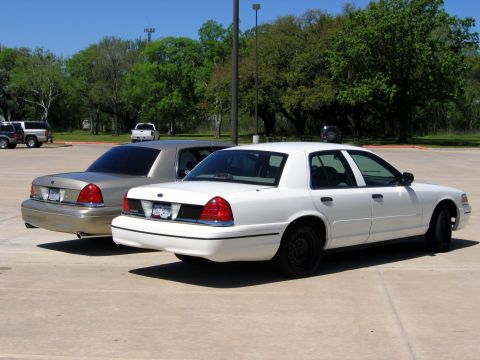 2000 Ford Crown Victoria - Two Ford Crown Victoria police cars are parked in a lot on a sunny day.