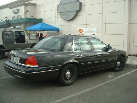 1999 Ford Crown Victoria - A black police car is parked in a lot near a building and a food truck.
