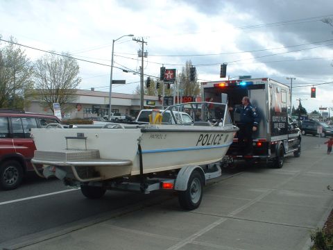 1999 Ford Crown Victoria - A police boat on a trailer is being towed by a truck, with a police officer standing by the truck's open door.