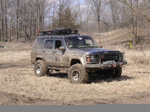 1995 Jeep Cherokee - A heavily muddied Jeep Cherokee navigates an off-road trail during the day.
