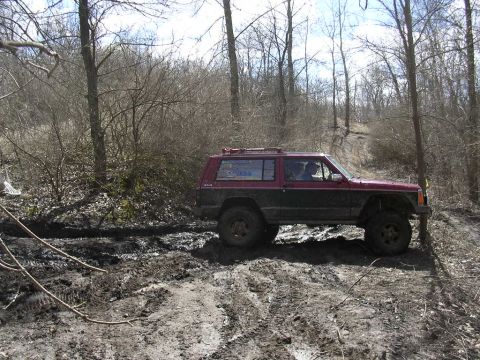 1995 Jeep Cherokee - A two-tone 1995 Jeep Cherokee navigates a muddy, wooded path.