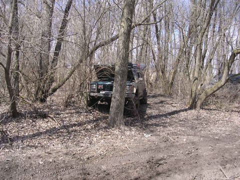 1995 Jeep Cherokee - A Jeep Cherokee sits in a muddy, wooded area with its hood up.