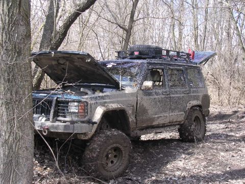 1995 Jeep Cherokee - Muddy 1995 Jeep Cherokee with hood up, parked off-road in a wooded area.