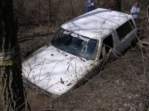 1995 Jeep Cherokee - A white Ford Bronco is stuck in a muddy ditch, with people observing from the background.