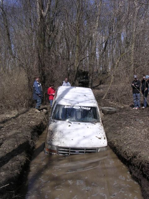 1995 Jeep Cherokee - A white Ford truck is stuck in a muddy ditch with people watching.
