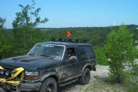 1993 Ford Bronco - Mud-covered 1993 Ford Bronco navigates an off-road trail with an orange flag on its roof rack.